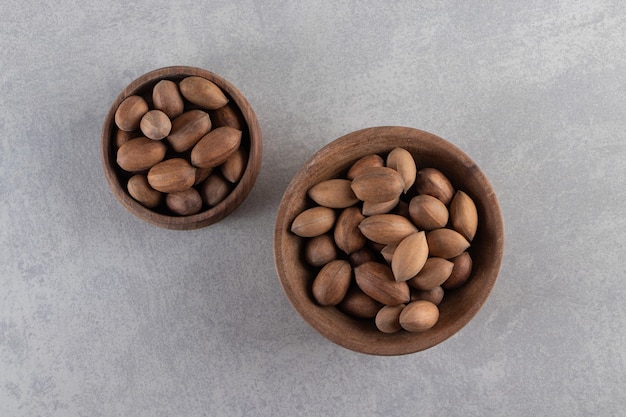 Cuencos de madera de nueces sin cáscara orgánicas sobre fondo de piedra.