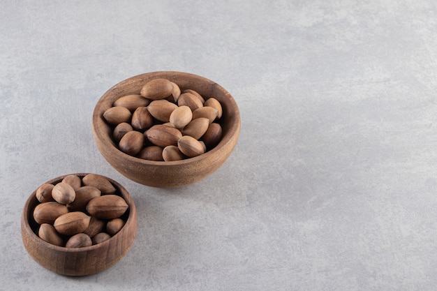 Cuencos de madera de nueces sin cáscara orgánicas sobre fondo de piedra.