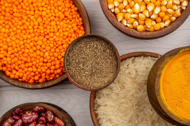 Cuencos de madera de vista superior con arroz semillas de calabaza lentejas de cúrcuma en polvo de pimienta negra sobre fondo gris