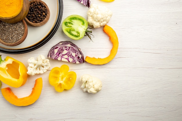 Foto gratuita cuencos de media vista superior con especias en plato redondo cortar verduras en espacio libre de mesa de madera blanca