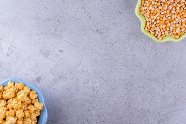 Foto gratuita cuencos opuestos alineados llenos de grano de maíz y un montón de palomitas de maíz con sabor a caramelo sobre fondo de mármol. foto de alta calidad