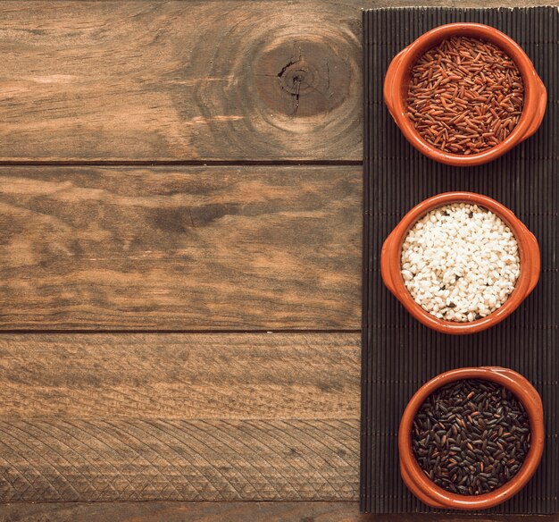 Cuencos orgánicos de los granos del arroz marrón y blanco en la bandeja sobre la tabla de madera