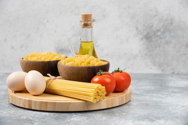 Cuencos de pasta cruda, huevos, tomates y aceite de oliva en la superficie de mármol.