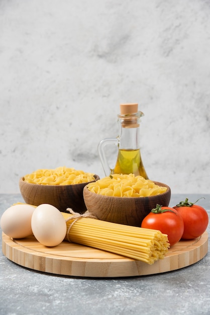 Cuencos de pasta cruda, huevos, tomates y aceite de oliva en la superficie de mármol.