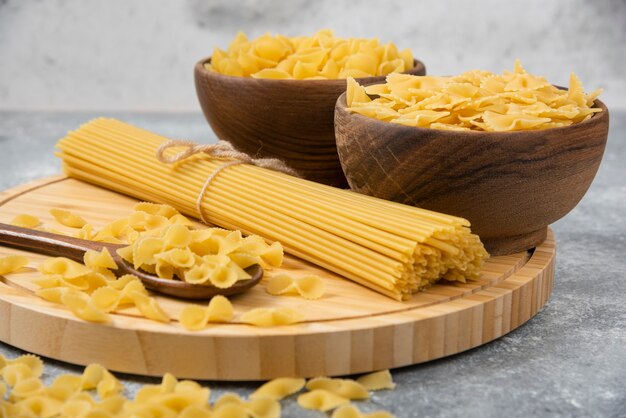 Cuencos de pasta seca cruda y espaguetis sobre superficie de mármol.