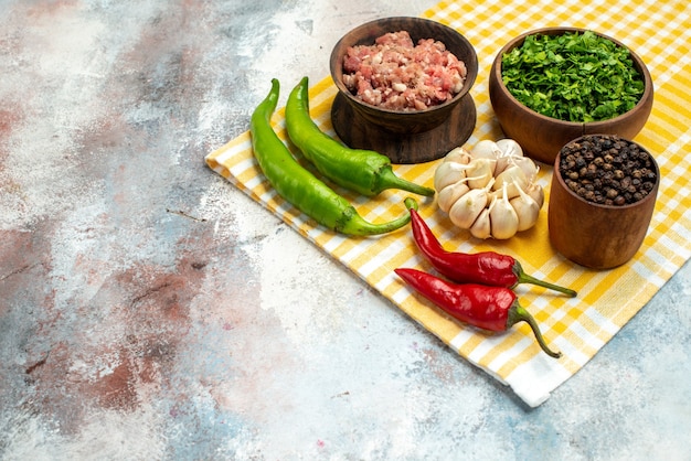 Cuencos de vista frontal con verduras de carne, pimienta negra, pimientos picantes, ajo en una toalla de cocina en un lugar libre de fondo desnudo