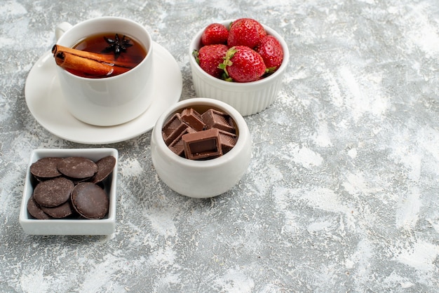 Foto gratuita cuencos de vista inferior con fresas y chocolates y té de semillas de anís y canela en la parte superior izquierda del fondo blanco grisáceo