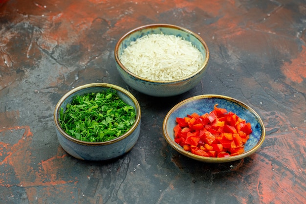 Cuencos de vista inferior con pimientos picados y arroz verde en la mesa de color rojo oscuro