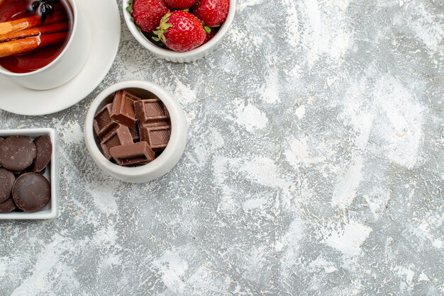 Cuencos de vista de la mitad superior con fresas y chocolates y té de semillas de anís y canela en la parte superior izquierda del suelo gris-blanco