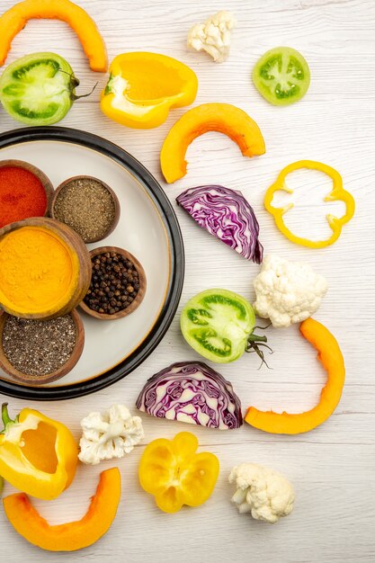 Foto gratuita cuencos de vista superior con especias en plato blanco verduras picadas sobre superficie blanca