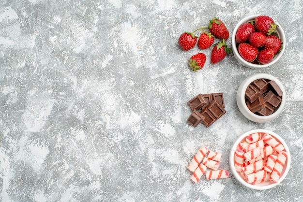 Foto gratuita cuencos de vista superior con fresas, chocolates, caramelos y algunas fresas, bombones, caramelos en el lado derecho del suelo gris-blanco.