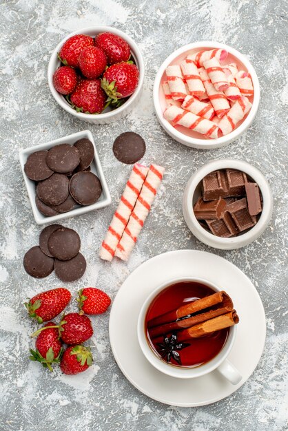 Cuencos de vista superior con fresas, chocolates, caramelos y té de semillas de anís y canela en el mosaico de suelo gris-blanco