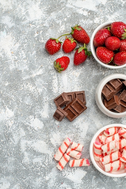 Foto gratuita cuencos de vista superior con fresas, chocolates, dulces y algunas fresas, chocolates, dulces en el lado derecho de la mesa gris-blanca.