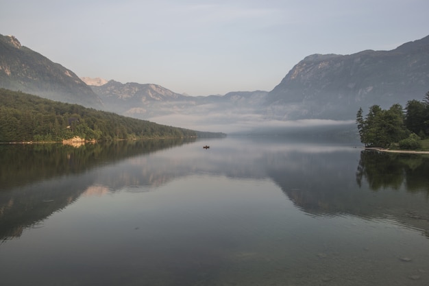 Cuerpo de agua cerca de cadenas montañosas con vegetación verde cubierta de niebla durante el día