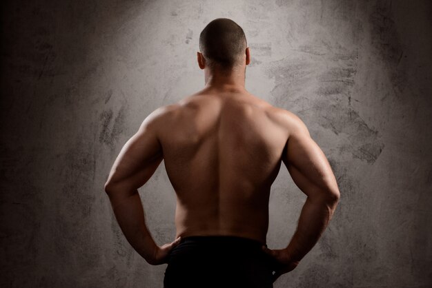 El cuerpo del hombre deportivo sobre la pared oscura.