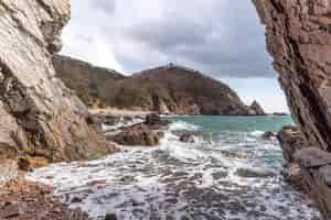 Foto gratuita cueva de playa con olas rompientes y colinas en el fondo contra un cielo nublado