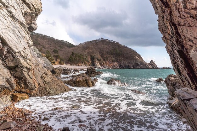 Cueva de playa con olas rompientes y colinas en el fondo contra un cielo nublado