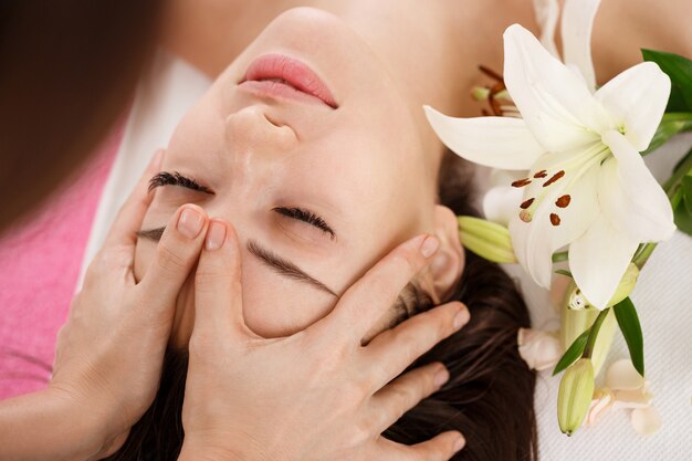 Cuidado de la piel y el cuerpo. Mujer joven recibiendo masaje facial. Belleza facial