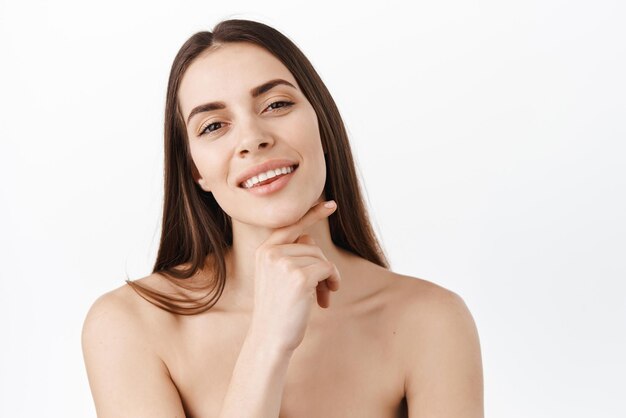 Cuidado de la piel Mujer con cara de belleza tocando retrato de piel facial saludable Hermosa modelo de niña sonriente con maquillaje natural tocando piel hidratada brillante sobre fondo rosa primer plano