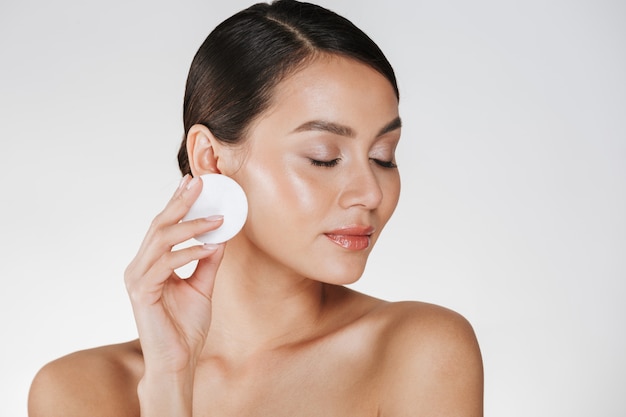 Cuidado de la piel y tratamiento saludable de la mujer que quita el maquillaje de la cara con un algodón, aislado en blanco