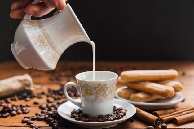 Cultive la mano vertiendo leche en la taza