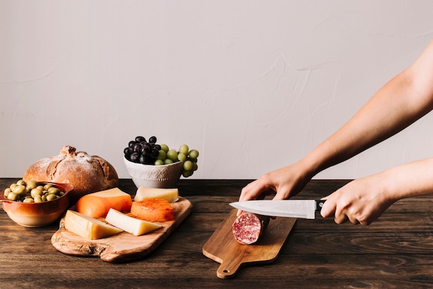 Cultive las manos cortando salchichas cerca de los alimentos