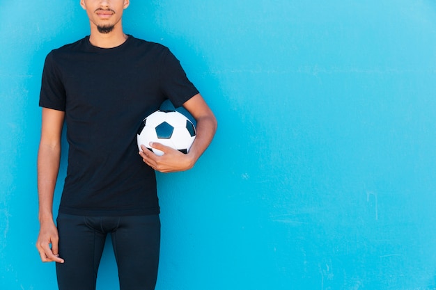 Cultivo de deportista étnico con balón de fútbol bajo el brazo.