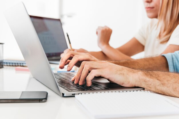 Cultivo de manos escribiendo en la computadora portátil en el lugar de trabajo