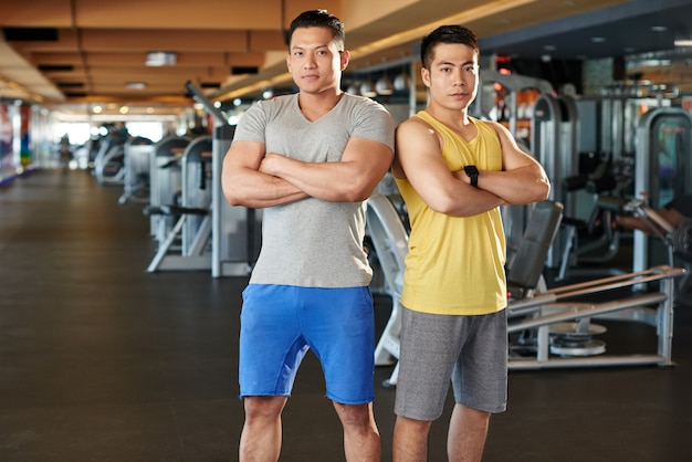 Culturistas de pie hombro con hombro en el gimnasio mostrando sus músculos