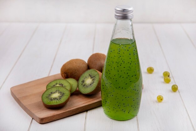 Cuñas de kiwi de vista frontal en la tabla de cortar con una botella de jugo en la pared blanca