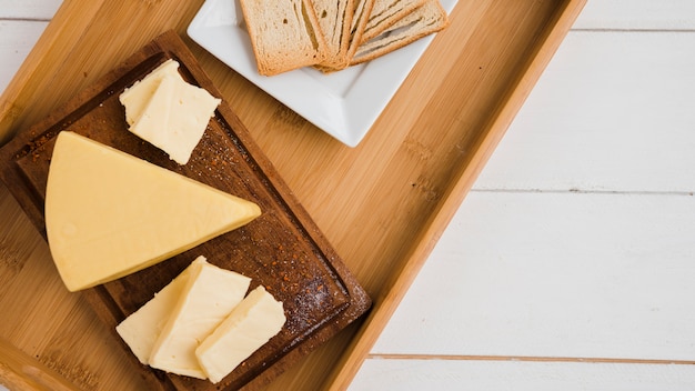 Cuñas de queso triangular en bandeja de madera contra el escritorio blanco