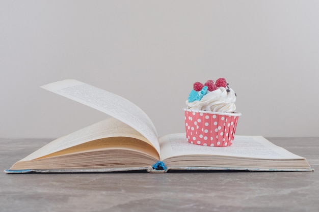 Un cupcake y un libro abierto sobre mármol.