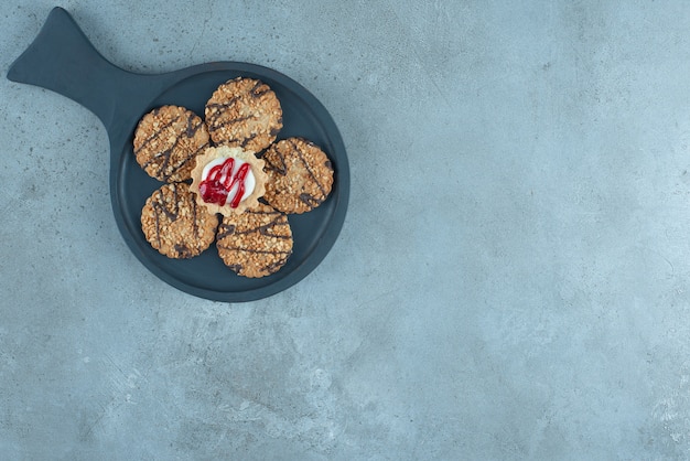 Foto gratuita cupcake rodeado de galletas en una bandeja pequeña sobre superficie de mármol