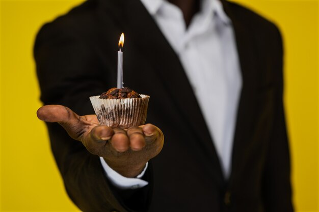 Cupcake con velas encendidas en la mano de afroamericanos en el fondo amarillo