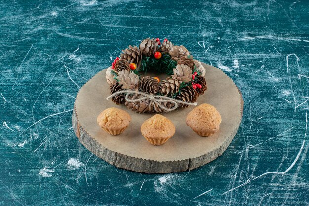 Cupcakes y una corona de pino dispuestas sobre una tabla de madera en azul.