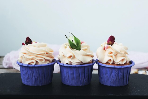 Cupcakes con delicada crema en un soporte lila, decorados con flores sobre una mesa blanca. Enfoque selectivo.