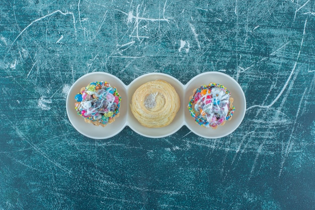 Cupcakes y una galleta en un plato pequeño sobre fondo azul. Foto de alta calidad