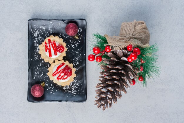 Cupcakes con salsa de fresa en bandeja negra, con adornos navideños sobre superficie de mármol