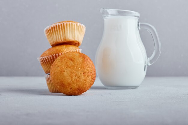 Cupcakes con un tarro de leche en superficie gris.