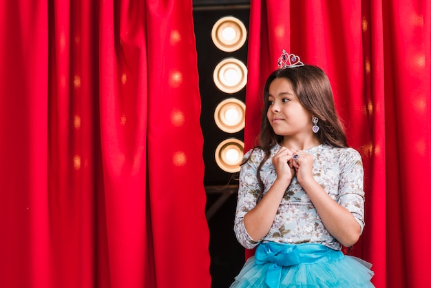 Curiosa chica linda de pie delante de la cortina roja mirando el escenario