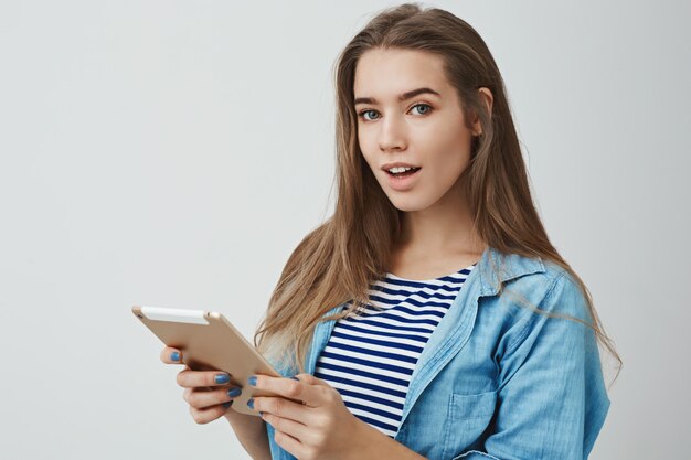 curiosa hermosa mujer joven moderna pelo largo y hermoso, boca abierta intrigada girando, sosteniendo tableta digital dorada, aprendiendo hechos interesantes en línea