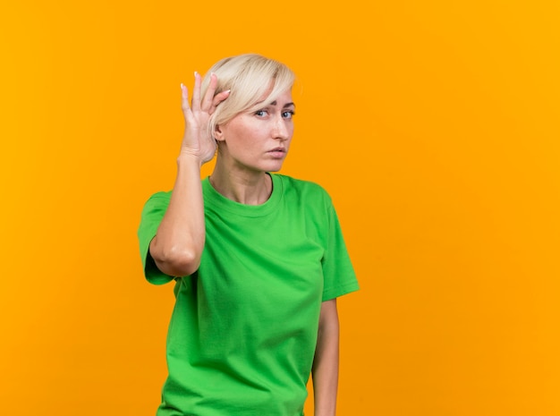 Foto gratuita curiosa mujer rubia de mediana edad mirando al frente haciendo no puedo oírte gesto aislado en la pared amarilla