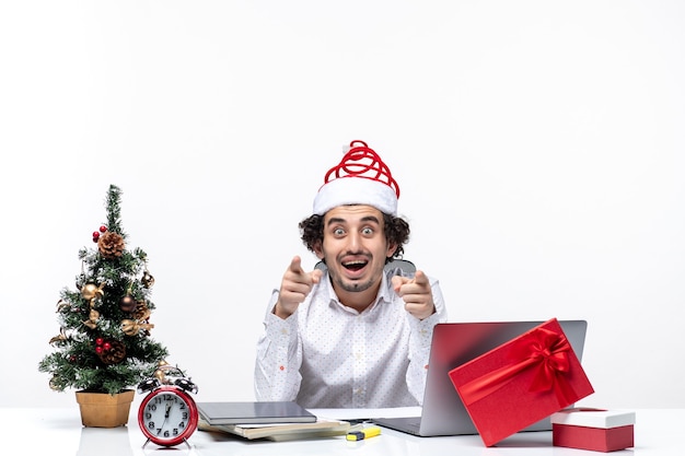 Curioso joven empresario con sombrero de santa claus divertido cuestionando algo en la oficina sobre fondo blanco.