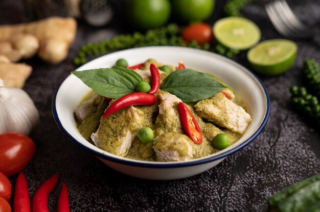 Curry de cerdo verde en un recipiente blanco con especias sobre un fondo de cemento negro