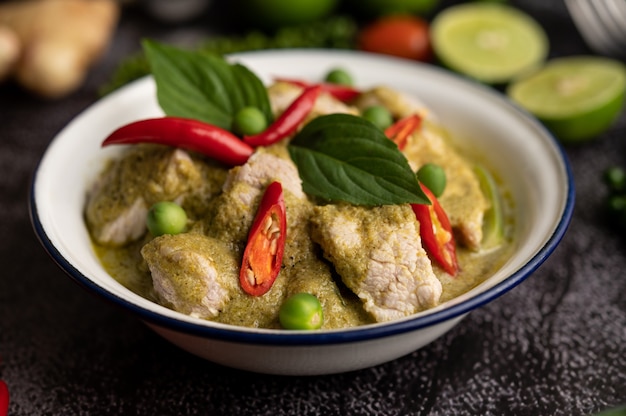 Curry de cerdo verde en un recipiente blanco con especias sobre un fondo de cemento negro