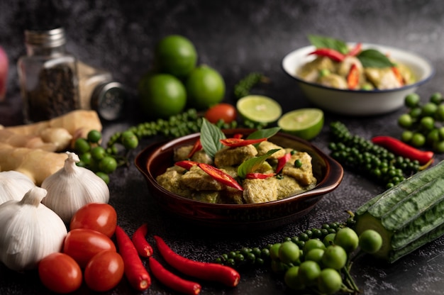 Curry de cerdo verde en un recipiente marrón con especias sobre un fondo de cemento negro