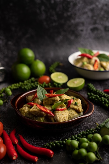 Curry de cerdo verde en un recipiente marrón con especias sobre un fondo de cemento negro