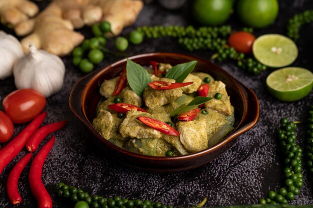 Curry de cerdo verde en un recipiente marrón con especias sobre un fondo de cemento negro