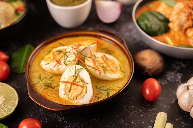 Curry verde con huevos en tazas negras, con limón, limoncillo, ají y tomates.