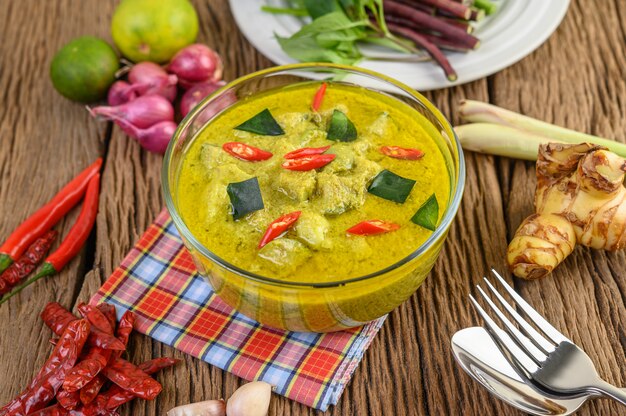 Curry verde en un recipiente con un tenedor y una cuchara en la mesa de madera.